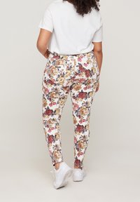 Leggings floreali bianchi con motivi di fiori multicolori. Design aderente con una texture liscia, abbinati a sneakers bianche e una maglietta semplice.