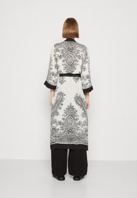 Long white kimono with black paisley patterns, 3/4 sleeves, and a black belt. Bottom has a black trim, worn over black loose pants.