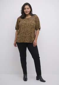 Blouse en imprimé léopard marron avec des manches courtes, coupe décontractée, assortie à un pantalon noir ajusté et des bottines noires. Design épuré et moderne.