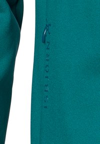 Teal langærmet beklædningsgenstand med glat tekstur. Har et synligt logo og brandnavn langs ærmet i en mørkere teal.