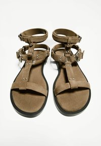 Sandaler med en övre del av brunt mockaskinn, med en öppen design, justerbara ankelremmar och metallnitar på remmarna. Sula av svart gummi.