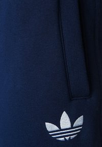 Mörkblå mjukisbyxor med en mjuk textur, utrustade med en sydd logotyp på vänster lår och ett elastiskt midjeband för komfort.