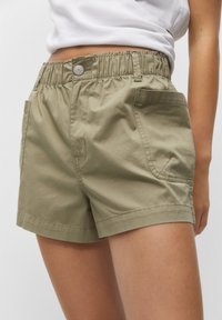 Shorts verts en coton avec une ceinture élastique, dotés de deux poches latérales et d'une texture lisse, coupés au-dessus du genou avec une coupe droite.
