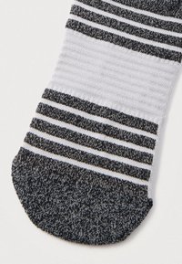 Μαύρη, λευκή και γκρι πλεκτή περιοχή δαχτύλων κάλτσας με οριζόντιες ρίγες και σκουρόχρωμη φτέρνα σε λευκό φόντο.