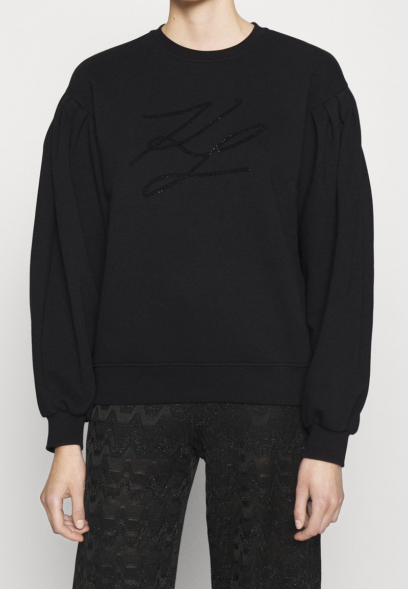 Sweat-shirt noir à enfiler avec des manches bouffantes et un logo noir texturé sur le devant. Confectionné dans un tissu doux avec une coupe ample.