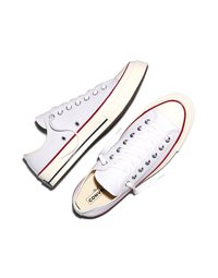 Pereche de teniși Converse albi cu talpă joasă, cu dungi roșii și negre pe tălpi, șireturi albe și ochiuri metalice, fotografiați de sus pe un fundal alb.