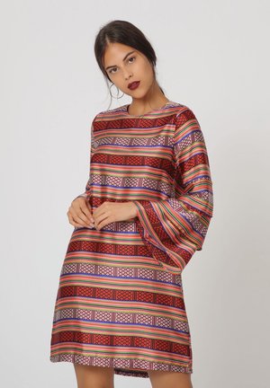 Mujer con un vestido de manga larga hasta la rodilla con rayas geométricas horizontales en rojo, naranja, púrpura y verde.