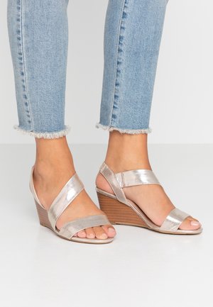 Wedge sandalen met metalen zilveren banden over de tenen en enkel, gecombineerd met lichtblauwe jeans met een rafelige zoom, voorzien van een houten wiggenhak.