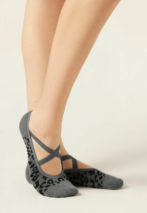 Feet wearing low-cut gray socks with black leopard print and elastic crisscross straps on a light background.