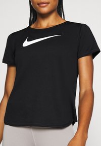 Czarna sportowa koszulka z krótkim rękawem i okrągłym dekoltem, z wyraźnym białym logo Nike na piersi, wykonana z oddychającej, teksturowanej tkaniny.