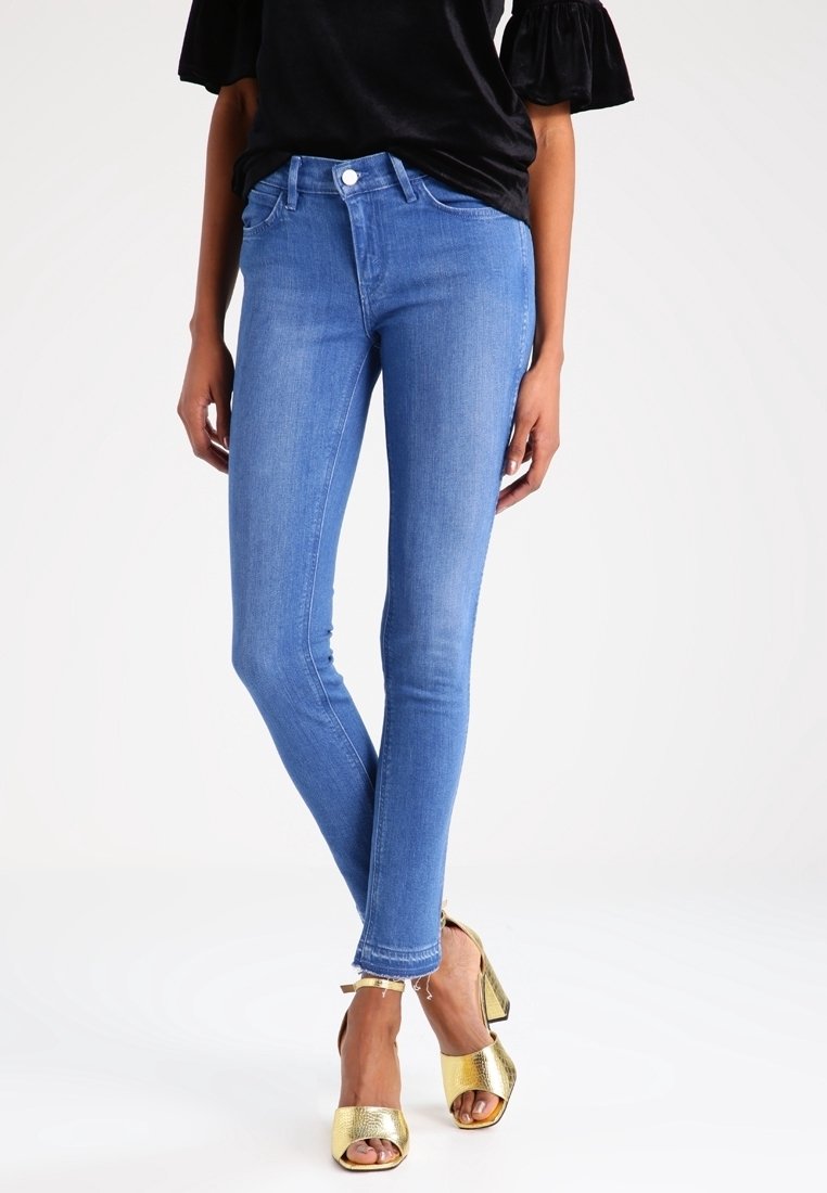 Jeans ajustados de mezclilla en color azul, con un diseño clásico de cinco bolsillos y un dobladillo deshilachado, combinados con zapatos de plataforma dorados.