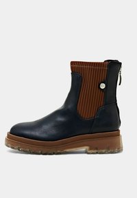 Bottine en cuir noir avec un panneau en tissu côtelé marron, une semelle épaisse couleur fauve et une fermeture éclair arrière avec languette.