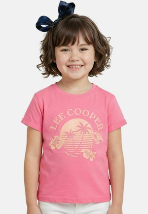 Jeune fille souriante aux cheveux bruns courts et portant un nœud noir, vêtue d'un t-shirt rose Lee Cooper orné d'un motif de palmiers et de fleurs.