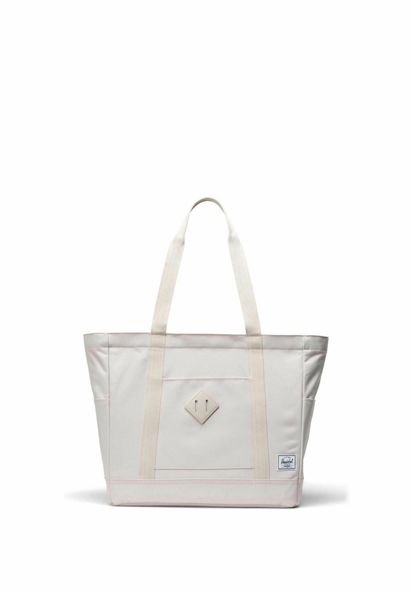 Sac fourre-tout en toile blanc cassé avec double bandoulière, poche avant, patch en forme de losange et petite étiquette de marque en bas à droite.