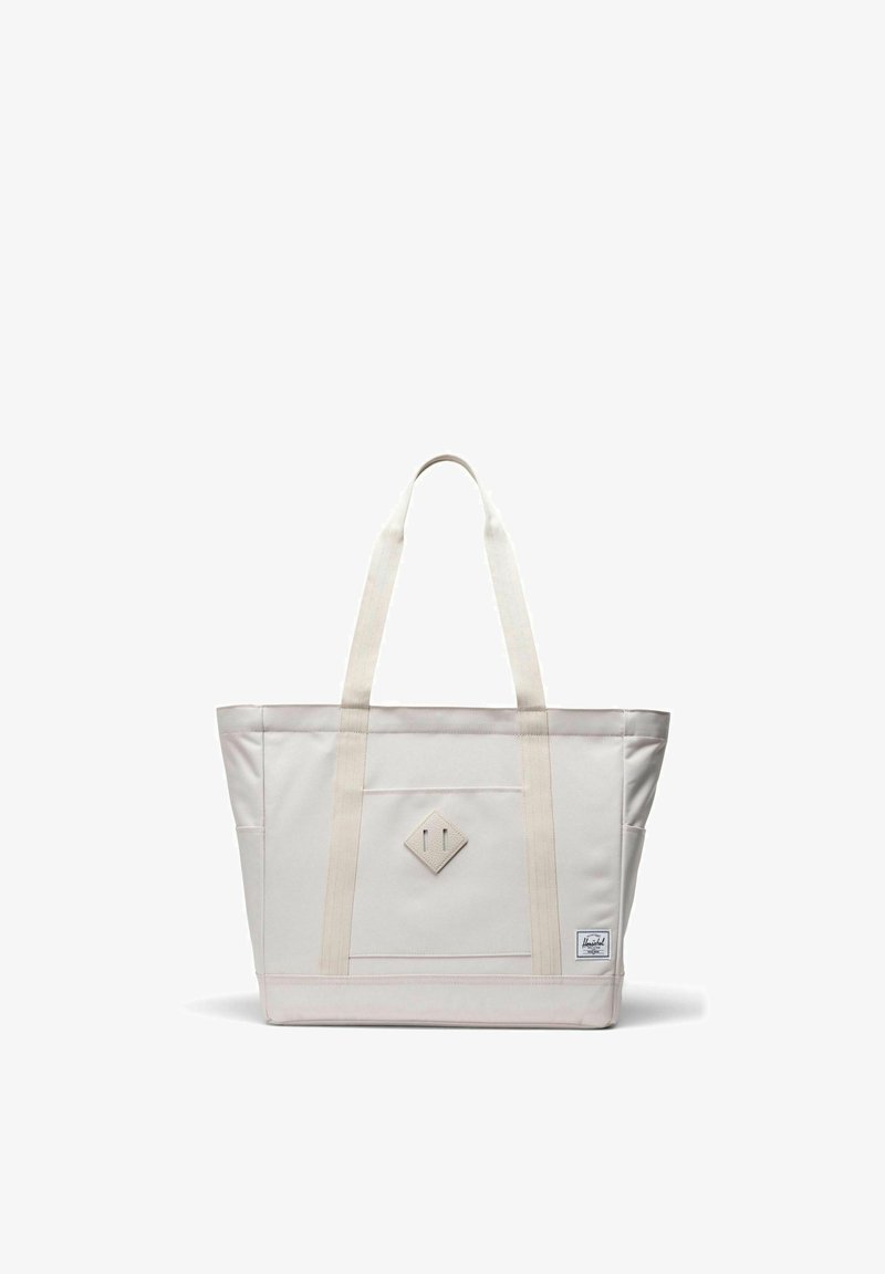 Sac fourre-tout en toile blanc cassé avec double bandoulière, poche avant, patch en forme de losange et petite étiquette de marque en bas à droite.