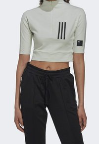Top corto verde claro con media cremallera, mangas cortas y diseño de tres franjas negras. Pantalones jogger negros con cinturilla ajustable.