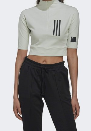 Hellgrünes, tailliertes Oberteil mit halbem Reißverschluss, kurzen Ärmeln und schwarzem Drei-Streifen-Design. Schwarze Jogginghose mit verstellbarem Bund.