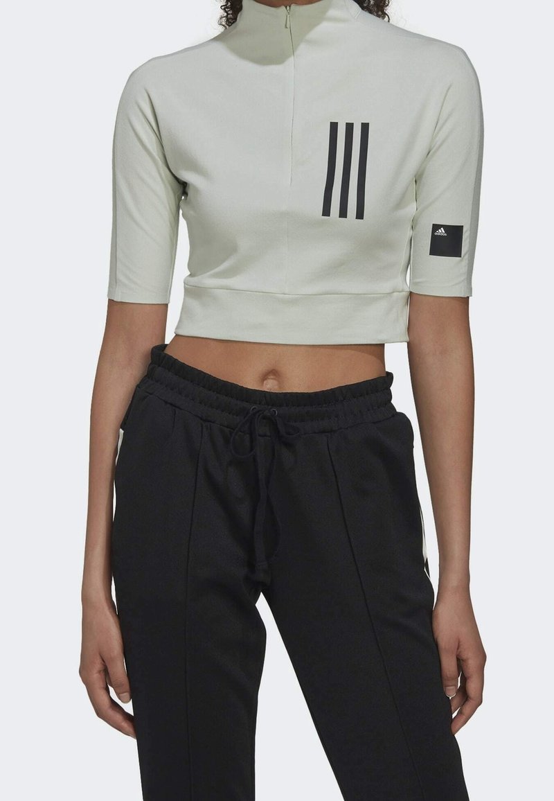 Top corto verde claro con media cremallera, mangas cortas y diseño de tres franjas negras. Pantalones jogger negros con cinturilla ajustable.