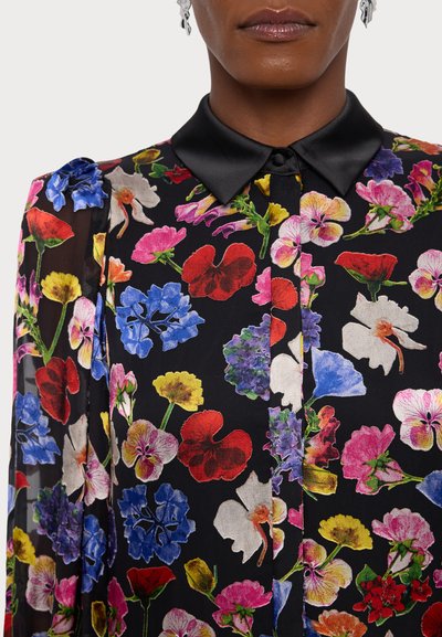 Blomstret bluse med sort baggrund, præget af flerfarvede blomstermønstre, en satin sort krave og gennemsigtige lange ærmer.