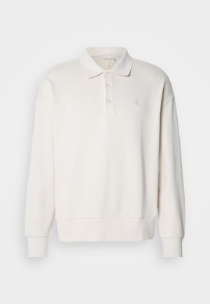 Elfenbensfarget longsleeve polo skjorte med ribbet tekstur, tre knapper på kragen og en subtil logo på venstre bryst.