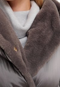 Chaqueta acolchada gris con un suave cuello de piel sintética y un cuello alto acanalado. Cuenta con un detalle de botón dorado en el cuello.