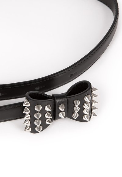 Zwarte leren riem met een strikvormig detail versierd met meerdere zilveren metalen spikes op een witte achtergrond.