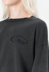 Zwarte oversized t-shirt gemaakt van zachte katoen, met een ronde hals en een subtiel geborduurd logo op de borst. Licht versleten textuur.