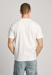 Camiseta de algodón blanca con mangas cortas y escote redondo. Textura suave, diseño sencillo, sin logotipos ni patrones visibles en la parte posterior.