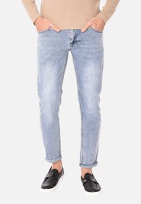 Jeans in denim azzurro chiaro con una vestibilità slim, dotati di cinque tasche e risvolti, abbinati a scarpe nere slip-on. Il materiale sembra morbido con un leggero lavaggio.
