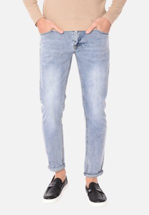 Jeans in denim azzurro chiaro con una vestibilità slim, dotati di cinque tasche e risvolti, abbinati a scarpe nere slip-on. Il materiale sembra morbido con un leggero lavaggio.