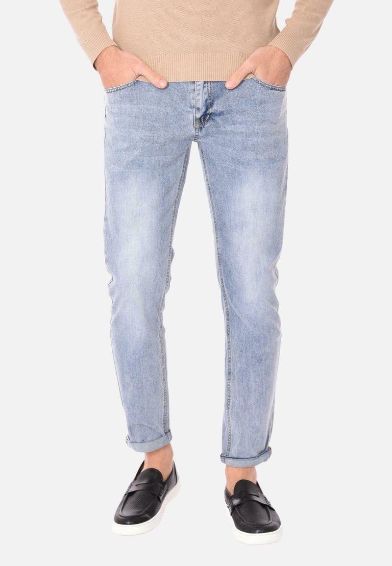 Jeans in denim azzurro chiaro con una vestibilità slim, dotati di cinque tasche e risvolti, abbinati a scarpe nere slip-on. Il materiale sembra morbido con un leggero lavaggio.