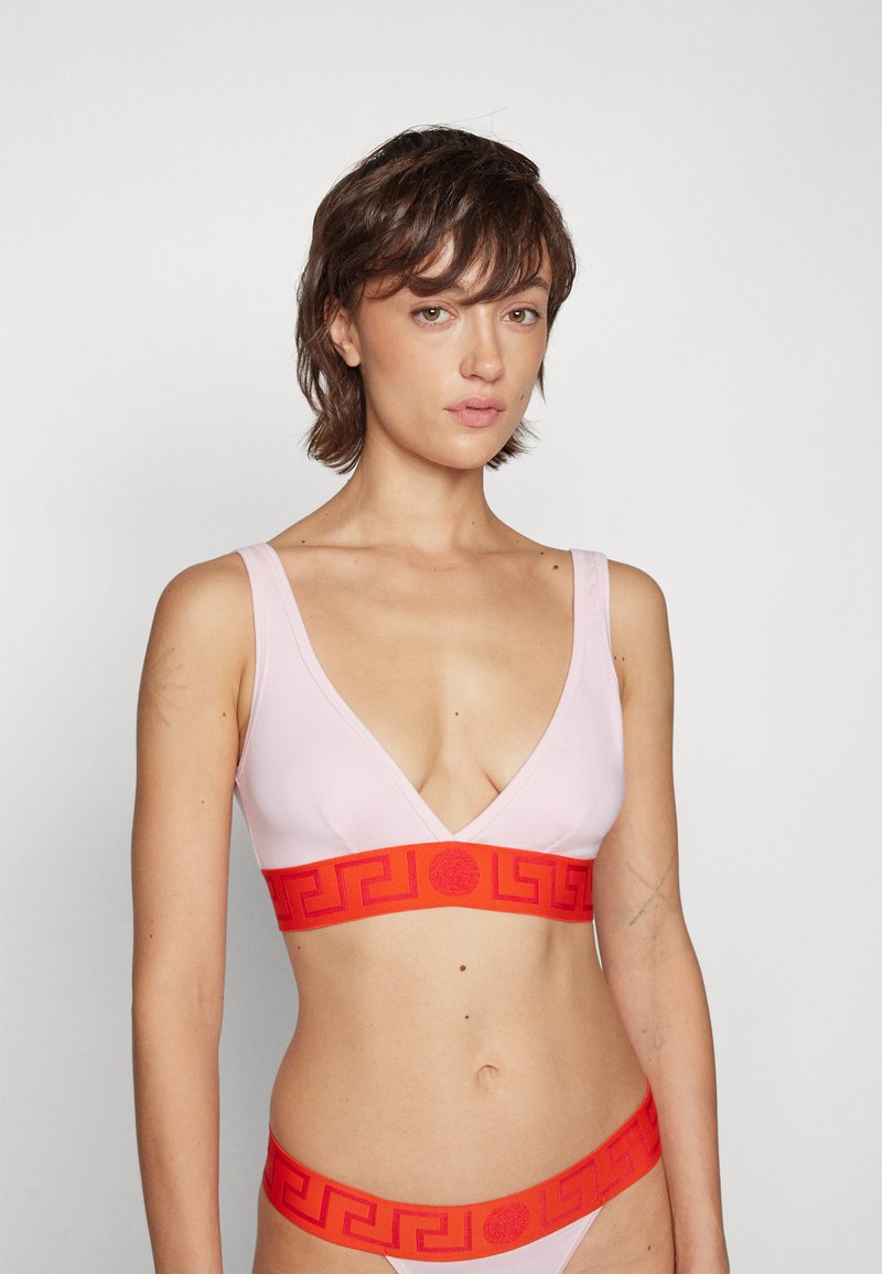 Pink bralette with a deep V-neck and matching high-waisted bikini bottom. Features a bold red elastic band with a Greek key pattern.
