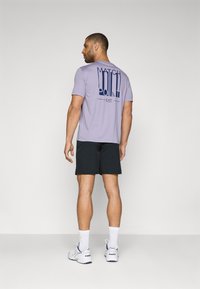 T-shirt lilás claro com gráfico "MATCH POINT" em azul marinho nas costas, combinado com calções pretos e ténis brancos. Textura suave, corte casual.