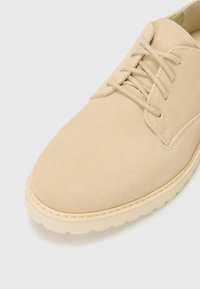 Beige suede shoe with a smooth texture, round toe, and lace-up design. Features a light-colored rubber sole and minimal stitching detail.
