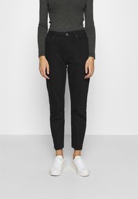 Crne traperice viskog struka slim fit kroja, s izrezanim rubom i suptilnim izblijedjenjem. Uparene s bijelim tenisicama i tamnopledastim topom dugih rukava.