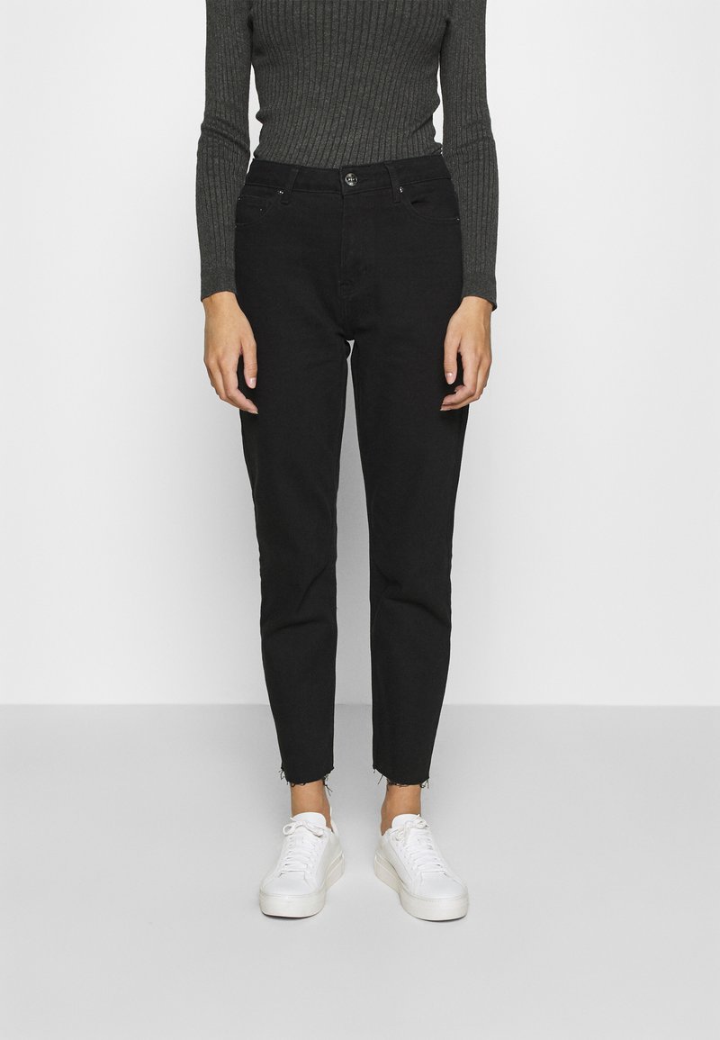 Crne traperice viskog struka slim fit kroja, s izrezanim rubom i suptilnim izblijedjenjem. Uparene s bijelim tenisicama i tamnopledastim topom dugih rukava.