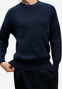 Suéter azul oscuro, acanalado, con cuello redondo, mangas largas y un corte holgado. La textura parece suave y tejida con ligeras variaciones.