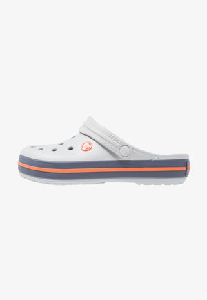 Jasnoszare klapki Crocs z otworami wentylacyjnymi, regulowanym paskiem na pięcie i granatową podeszwą z pomarańczowym paskiem.
