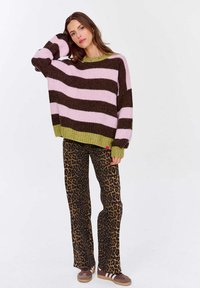 Sweter w paski w kolorze różowym i brązowym z zielonymi akcentami, połączony z brązowymi spodniami w panterkę z rozkloszowanym dołem oraz brązowymi trampkami.