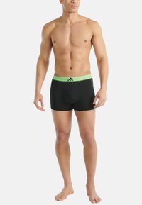 Svarta boxershorts gjorda av elastisk tyg med ett grönt elastiskt midjeband som har en logotyp. Slät textur, figurnära design, längd till mitten av låret.