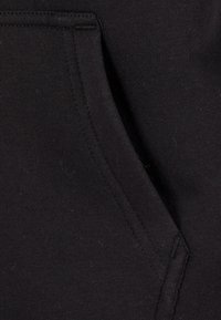 Black fabric with smooth texture, featuring a side pocket with a visible seam and stitching detail. The fabric appears lightweight and flexible.