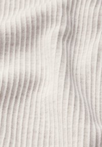 Helles beiges Gewebe mit einer weichen Textur, das vertikale Rippmuster aufweist. Das Material wirkt leicht und leicht flauschig.
