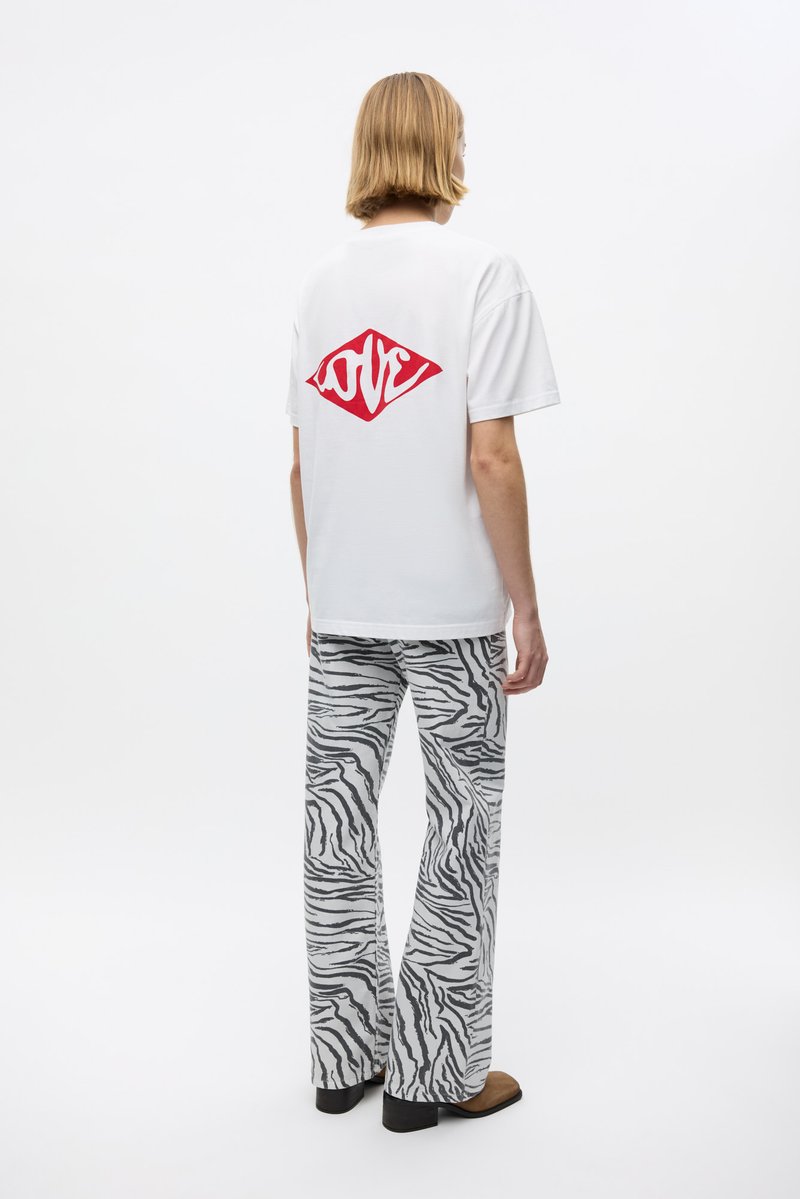 Camiseta de algodón blanca con gráfico rojo de "LOVE" en la parte de atrás, combinada con pantalones acampanados a rayas grises y negros. Se muestran zapatos planos.