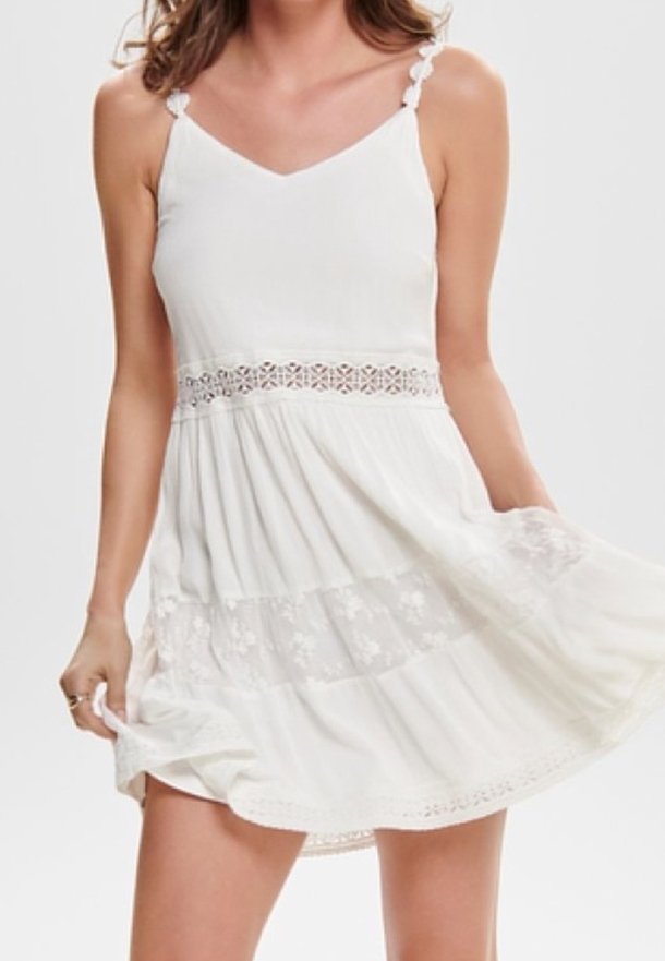 Vit sommarklänning med spaghetti-band, figurnära överdel, intrikata spetsdetaljer vid midjan och lager av kjol med blommönster.