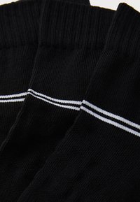 Schwarze Socken mit gerippter Textur und einem weißen Doppelstreifen am Bündchen. Hergestellt aus weichem, elastischem Material, das für Komfort sorgt.