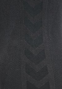 Zwart gebreid stof met een textuurpatroon dat chevronvormen vertoont. Het oppervlak heeft een lichte glans en een consistente, gladde textuur.