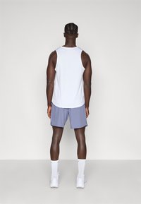 Top atlético sin mangas blanco, pantalones cortos azul claro, calcetines blancos y zapatillas; textura visible en la tela, diseñado para ropa deportiva.