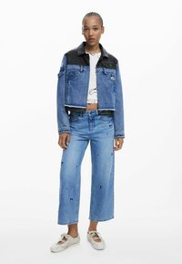Denim jacket with black leather collar, cropped design; light blue wide-leg jeans with embroidered accents; white sneakers with straps.