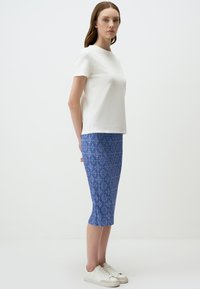 T-shirt blanc à manches courtes associé à une jupe crayon bleue à motifs, complété par des baskets blanches. Tissu lisse et design ajusté.