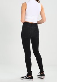 Jeans skinny negros con una alta cintura, que cuentan con dos bolsillos traseros y una textura clásica de denim, combinados con zapatillas negras.
